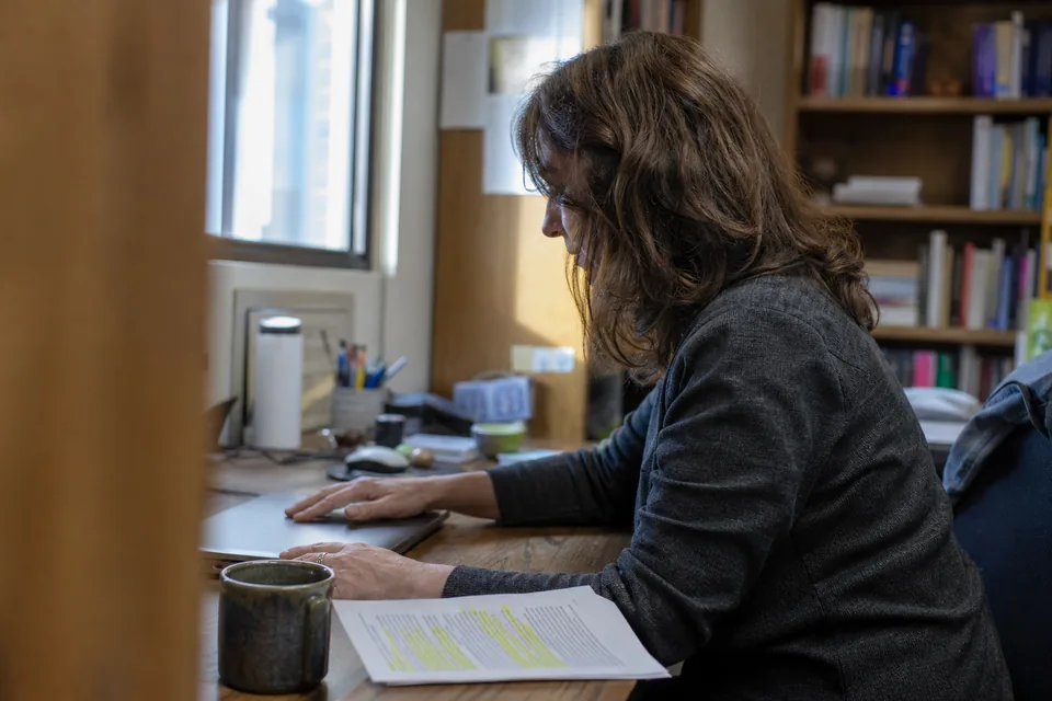 College professor at an office desk with a laptop and a highlighted printed lecture handout