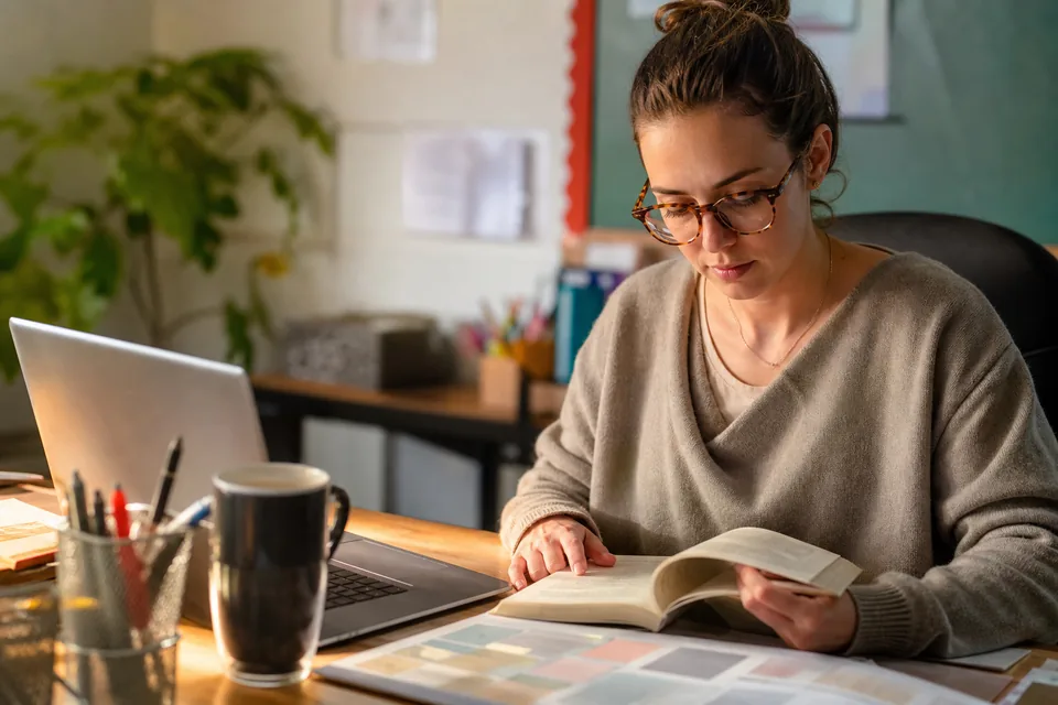 Teacher lesson planning with a novel, printed answer key and laptop