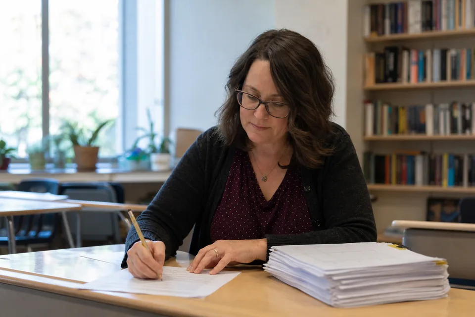 English teacher marking a printed reading passage at her classroom desk